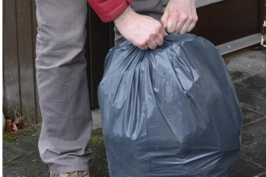 Image of man's hands tying up a black plastic garbage bag.