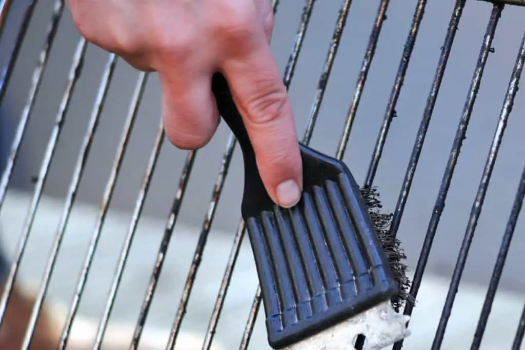 Hand holding a grill brush, scrubbing a Traeger grill grate.